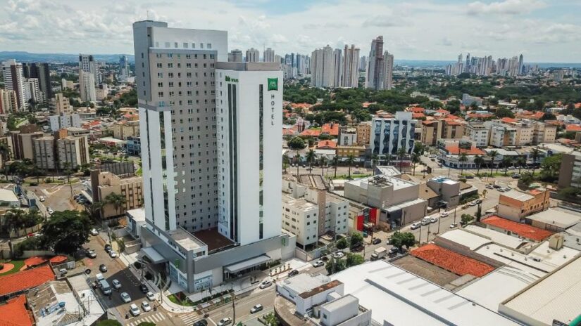 Um prédio alto e moderno de hotel em uma cidade movimentada com muitos arranha-céus e casas sob um céu nublado.