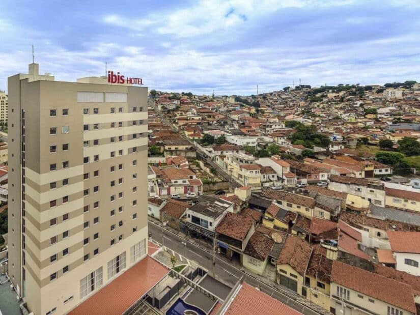 Alto edifício do hotel Ibis ao lado de um bairro densamente povoado com casas de telhado vermelho sob um céu nublado.