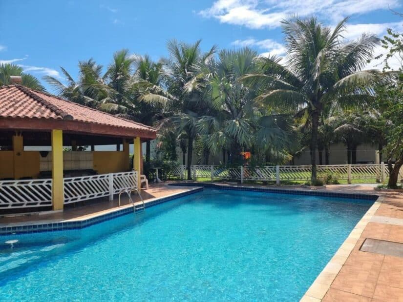 Uma piscina ao lado de um bar, cercada por palmeiras sob um céu azul brilhante.