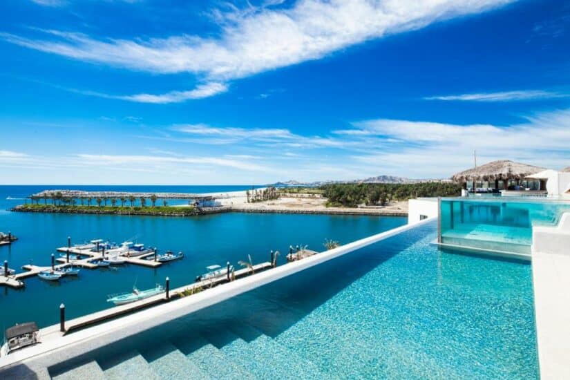 Piscina de borda infinita com vista para uma marina com barcos, água azul e um céu limpo em um dia ensolarado.