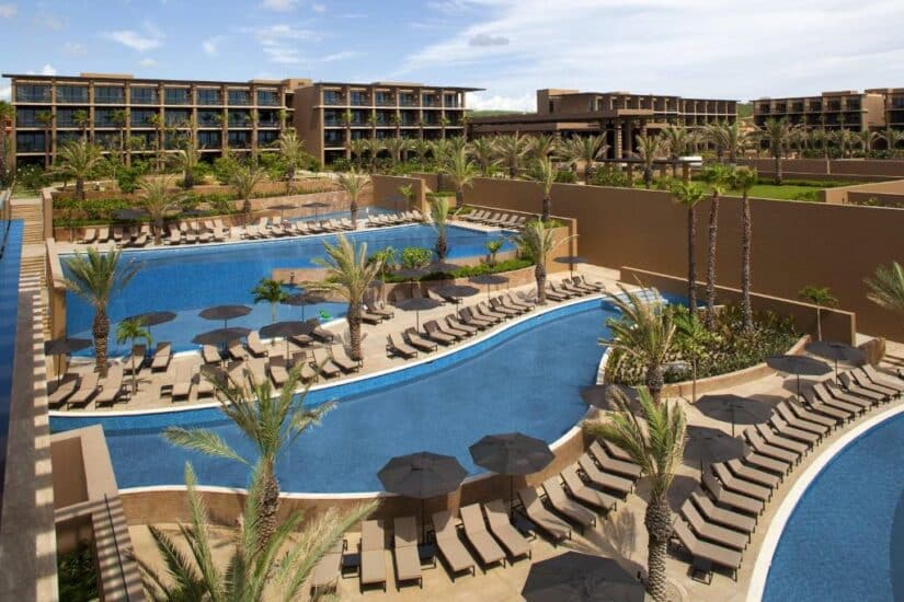 Grande resort onde ficar em Los Cabos com várias piscinas externas, espreguiçadeiras, palmeiras e modernos edifícios do hotel.