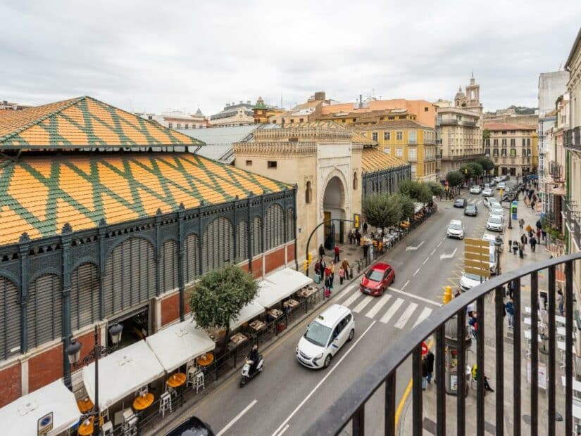 Uma rua movimentada ao lado de um edifício de mercado com telhas padronizadas e cafés ao ar livre onde ficar em Málaga sob um céu nublado.