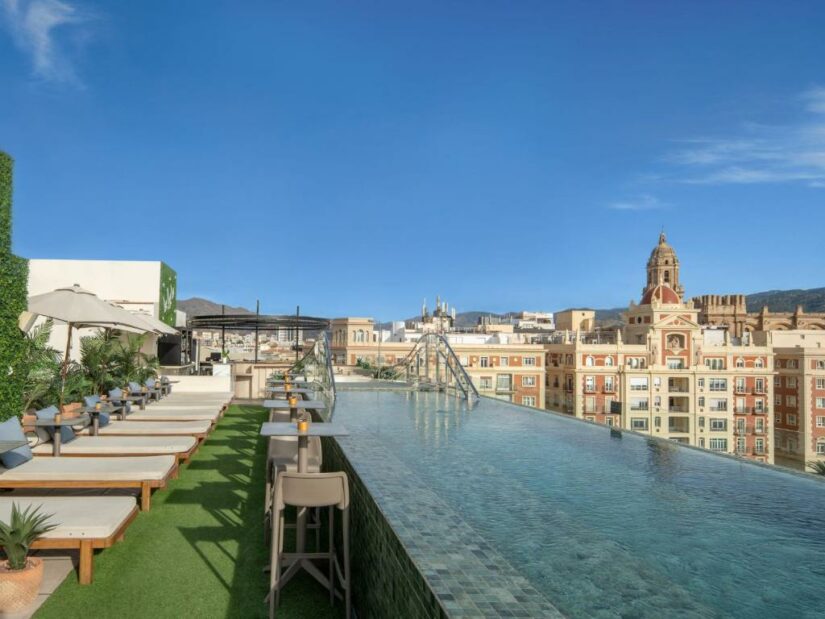 Piscina infinita na cobertura com espreguiçadeiras com vista para a paisagem urbana sob um céu azul claro.