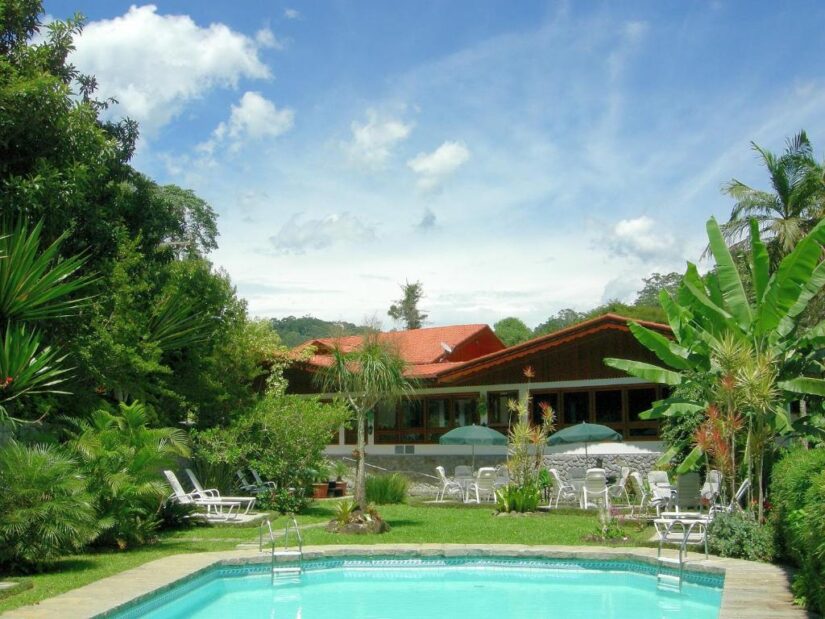 onde ficar em Nova Friburgo em Mury RJ Um jardim exuberante com piscina e uma casa de telhado vermelho — descubra os melhores hotéis em Mury no Rio de Janeiro sob um céu azul brilhante.