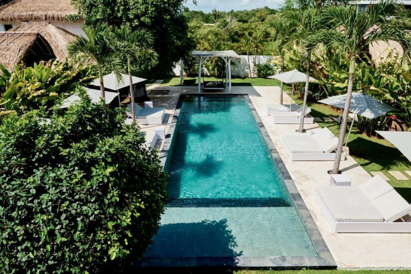Piscina externa retangular cercada por palmeiras Onde ficar em Uluwatu, espreguiçadeiras e guarda-sóis em um ambiente tropical.