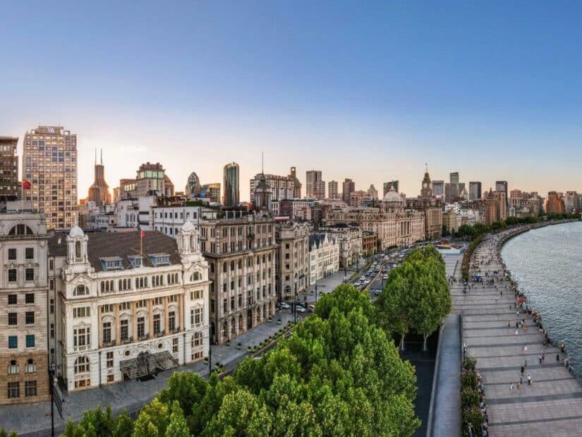 Vista panorâmica do Bund, onde ficar em Xangai, com edifícios históricos e um calçadão ao longo do rio ao pôr do sol.