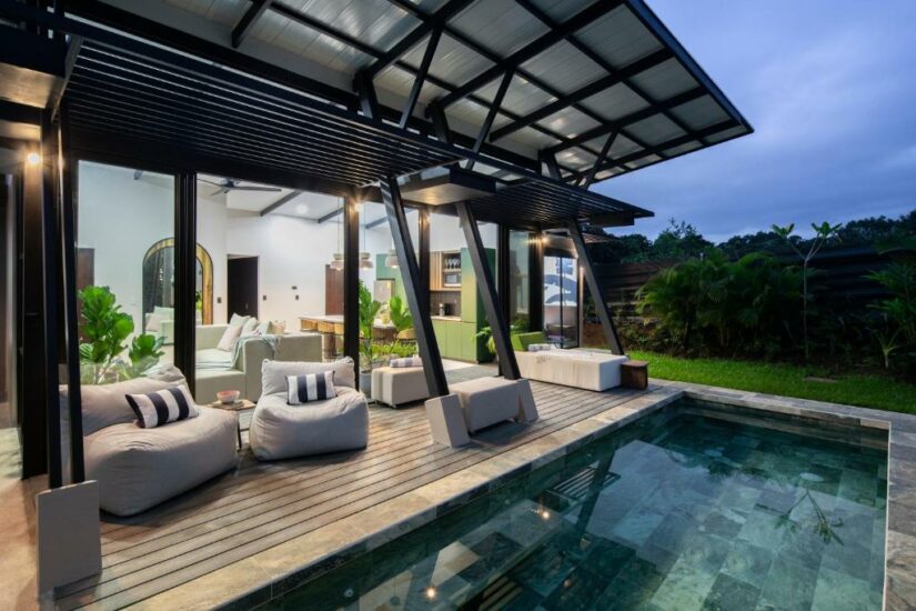 Pátio moderno com assentos no lounge e uma pequena piscina, cercado por vegetação e arquitetura contemporânea ao anoitecer.