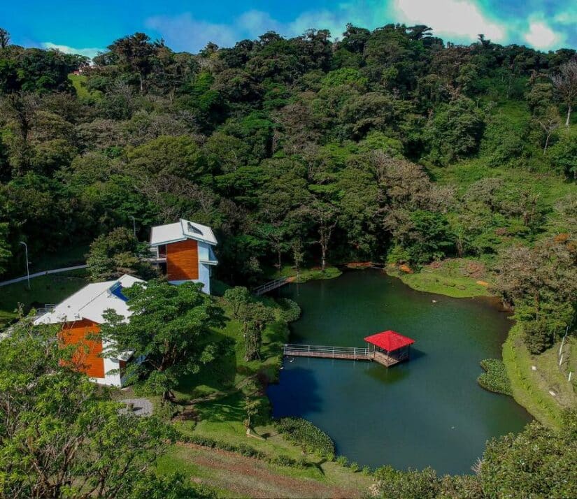 Uma casa branca com uma doca de telhado vermelho onde ficar na Costa Rica fica à beira de um pequeno lago, cercada por uma densa floresta verde.