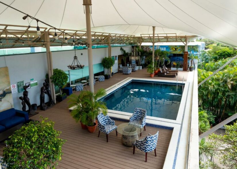 Piscina na cobertura onde ficar na Costa Rica com poltronas azuis, mesas, plantas e cobertura branca em um deck de madeira.