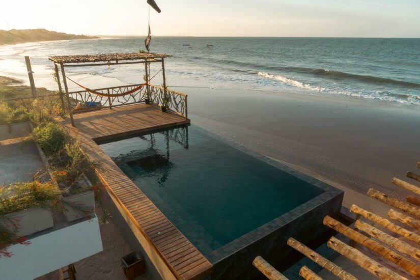 onde ficar em Icaraizinho de Amontada no Ceará Piscina infinita com deck de madeira e rede com vista para uma praia de areia e para o oceano ao pôr do sol.