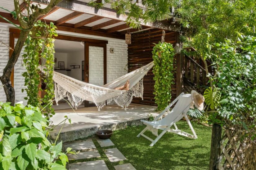 onde ficar em Icaraizinho de Amontada no Ceará Uma rede aconchegante em um pátio sombreado com vegetação, ao lado de uma espreguiçadeira branca e um chapéu de sol.