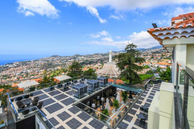 hotéis em Monte em Funchal na Ilha da Madeira em Portugal Telhado com painéis solares com vista onde ficar em Funchal, colinas e uma igreja circular branca sob um céu azul.
