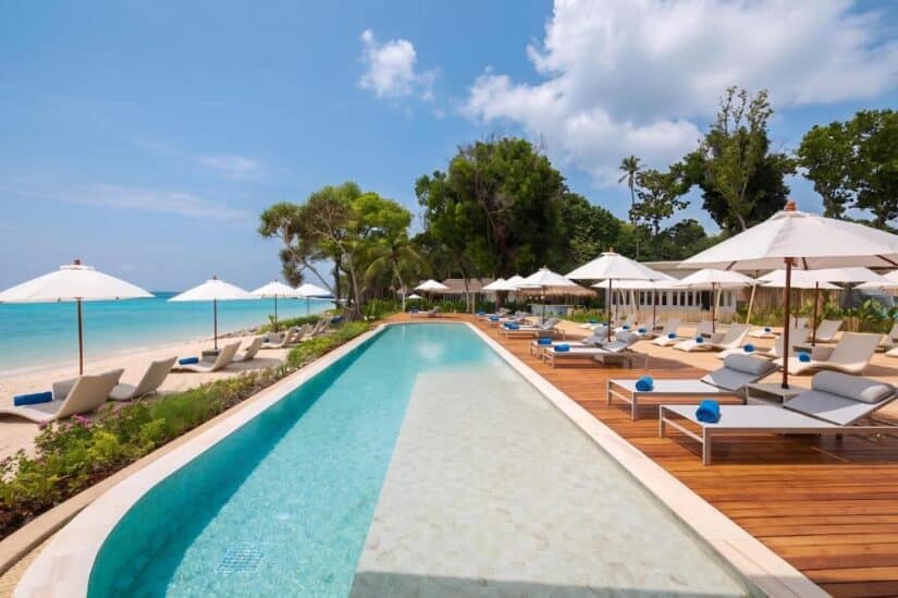 onde ficar em Koh Phi Phi na Tailândia Resort em uma praia ensolarada da Tailândia com piscina, espreguiçadeiras, guarda-sóis e um mar azul cristalino sob um céu parcialmente nublado.