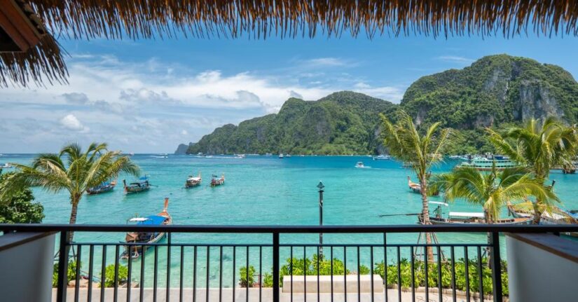 resorts beira-mar na Tailândia Vista da varanda de onde ficar em Koh Phi Phi: águas turquesa, barcos, palmeiras e montanhas verdes sob um céu azul com nuvens.