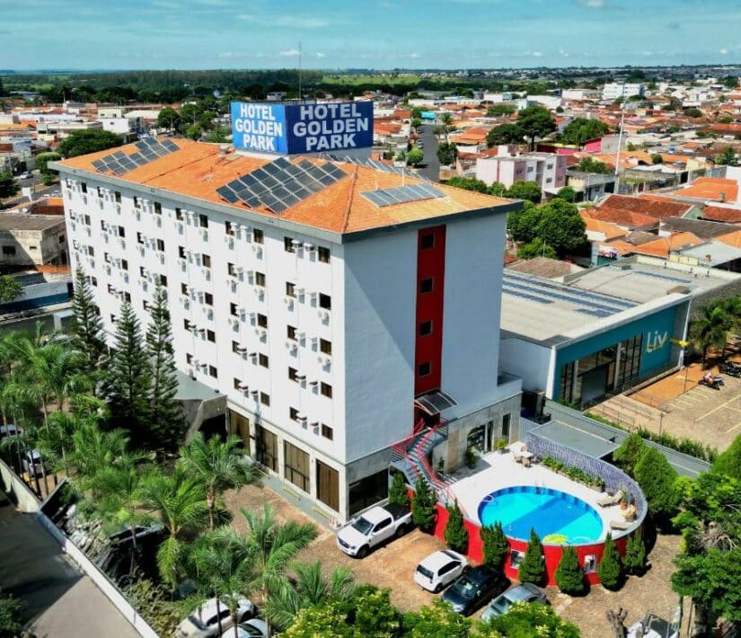 Vista aérea do Hotel Golden Park onde ficar em Rifaina com uma piscina, palmeiras e carros estacionados em uma área suburbana.