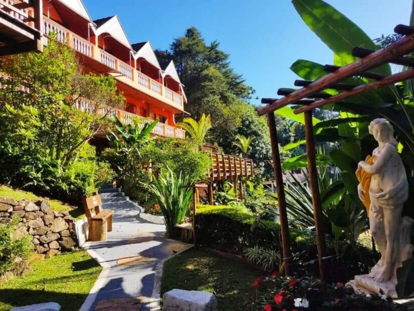 onde ficar em São Bento do Sapucaí em São Paulo Um caminho no jardim leva a um hotel de madeira com varandas, cercado por uma vegetação exuberante e uma estátua de mármore.
