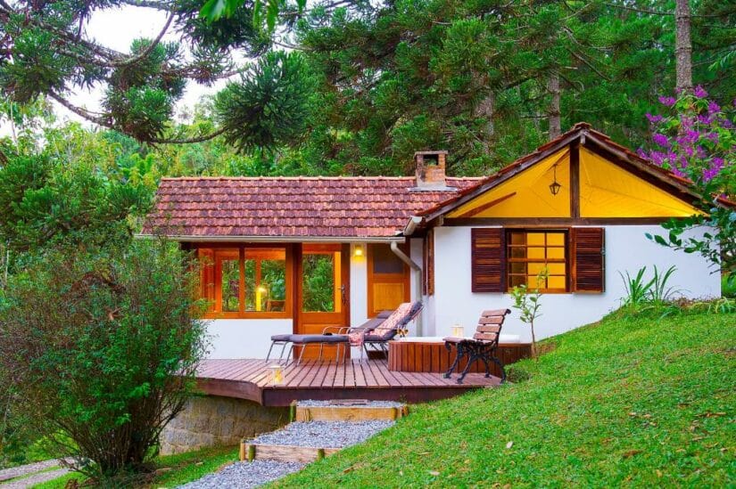 Um chalé aconchegante onde ficar em Visconde de Mauá com um deck de madeira, cercado por vegetação e árvores, com iluminação interna aconchegante.