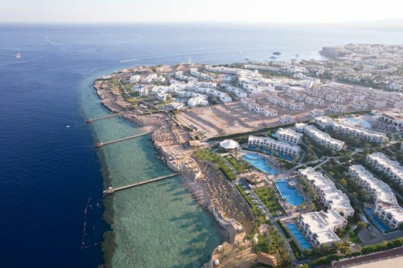 onde ficar em Sharm el Sheikh Hadaba no Egito Vista aérea de um resort à beira-mar com piscinas, edifícios brancos e um litoral azul claro.