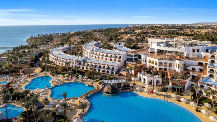 resorts na Sharks Bay no Egito Vista aérea de um grande resort onde ficar em Sharm el Sheikh à beira-mar com piscinas, prédios brancos e palmeiras perto da costa.