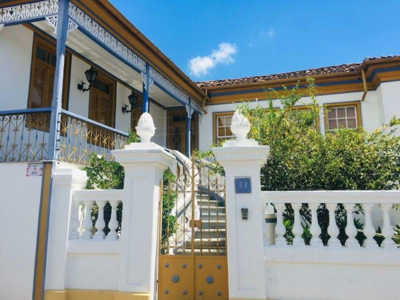 hotéis e pousadas em Diamantina Minas Gerais Casa branca em estilo colonial onde ficar em Diamantina com detalhes em dourado, portão de ferro e vegetação sob um céu azul brilhante.