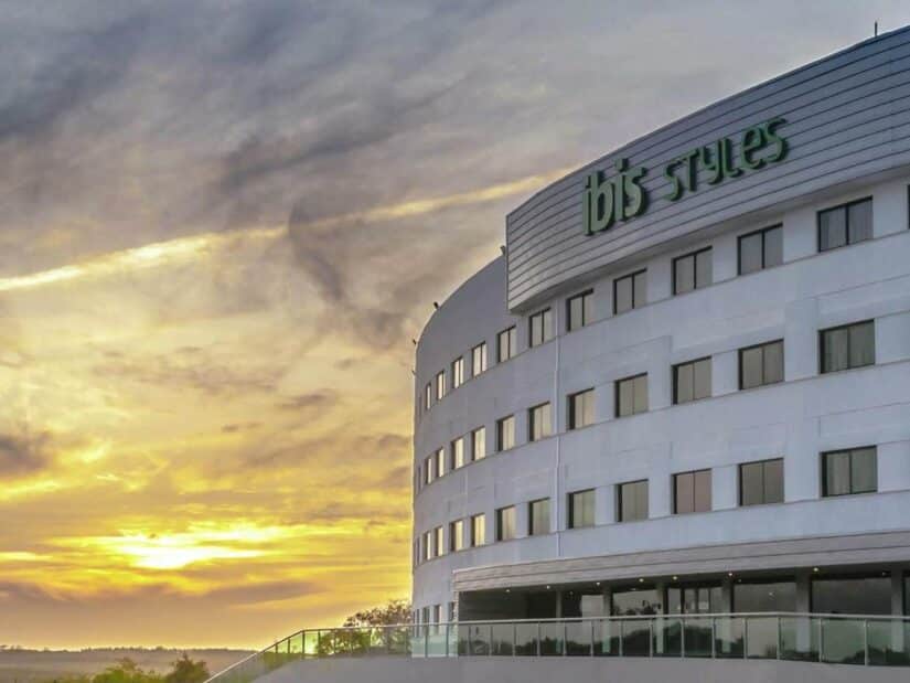 Edifício moderno de hotel branco com placa do ibis Styles ao pôr do sol, com nuvens dramáticas no céu onde ficar em Itaúnas .