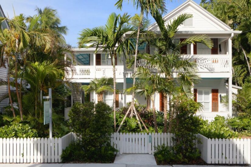 Casa de madeira branca com persianas, palmeiras e uma cerca branca na frente onde ficar em Key West.