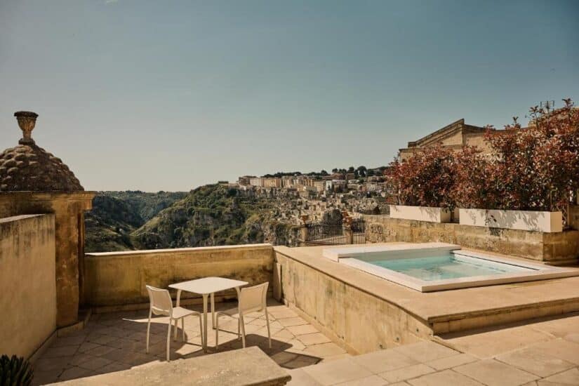 hotéis no sassi de Matera na Itália Um terraço ensolarado onde ficar em Matera com uma pequena piscina, mesa e cadeiras tem vista para uma cidade e um vale na encosta.