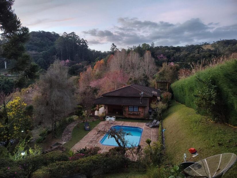 Onde se hospedar em Santo Antônio do Pinhal: casa com piscina cercada por colinas verdes, árvores e folhagens coloridas.
