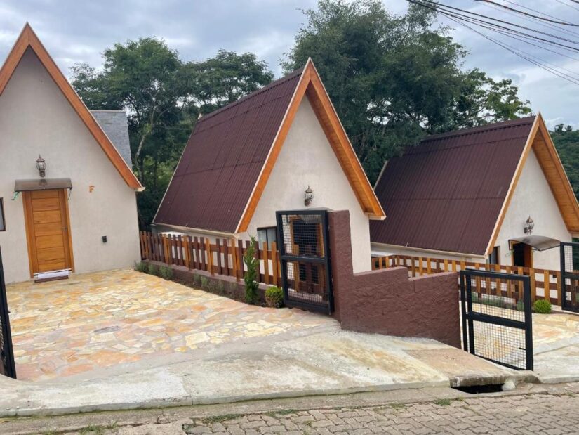 Três casas em forma de A com telhados marrons perto de árvores e de uma cerca; onde ficar em Santo Antônio do Pinhal.