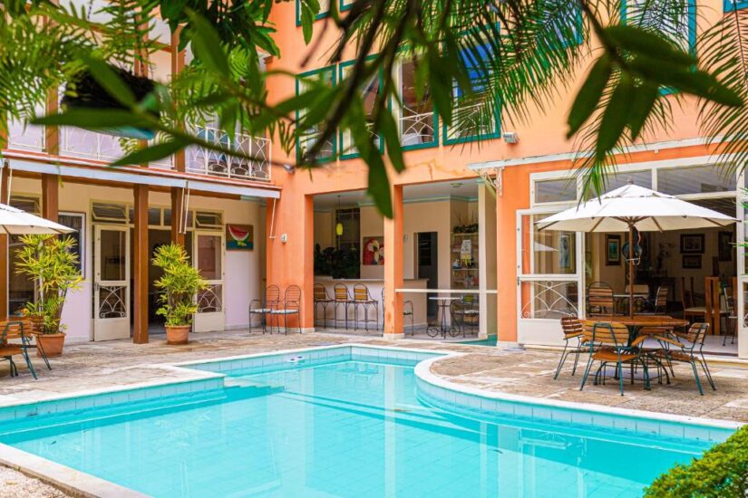 Uma piscina de águas azuis cristalinas, cercada por mesas e plantas em um pátio ensolarado — um lugar ideal para se hospedar em São João del Rei.