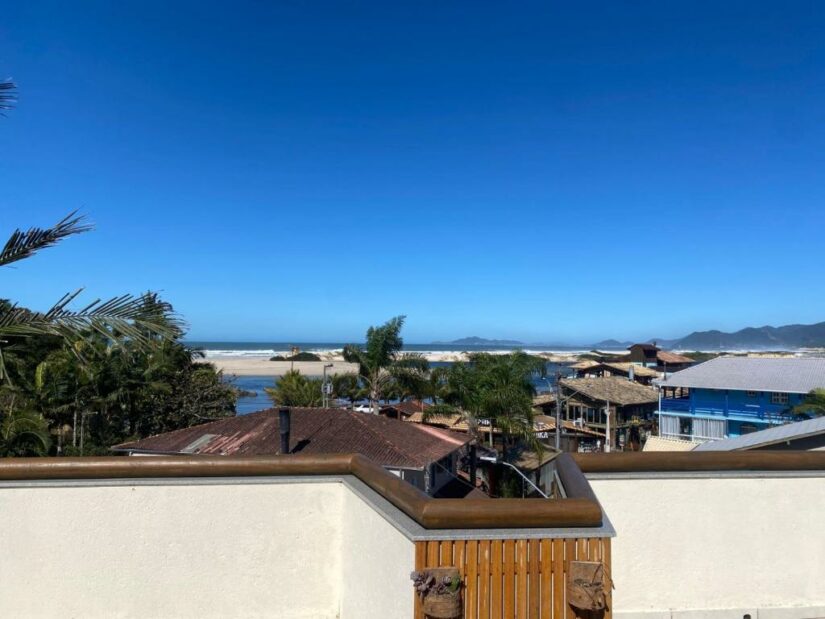 onde ficar na Guarda do Embaú e Pedra do Urubu em Santa Catarina Vista da praia e do oceano com céu azul, palmeiras e casas em primeiro plano.