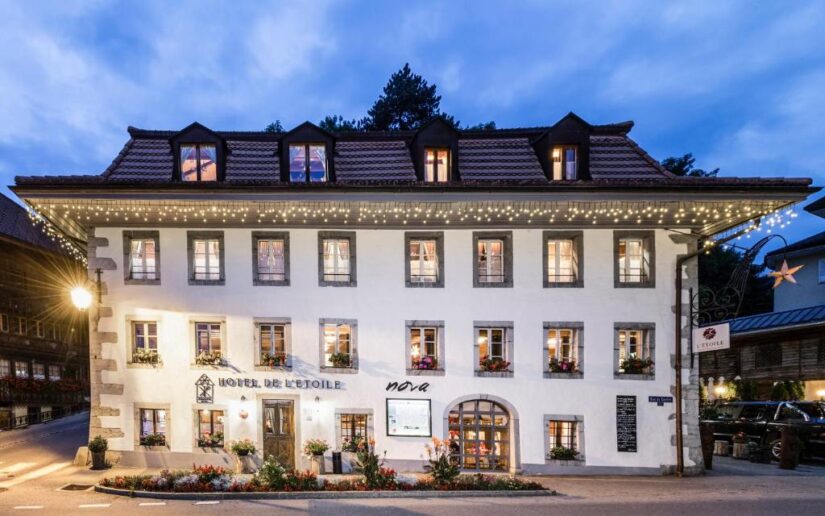 hotéis em Charmey na Suíça perto de Gruyères Um charmoso hotel branco onde ficar em Gruyères com floreiras e luzes de corda brilhando ao anoitecer em uma esquina tranquila.