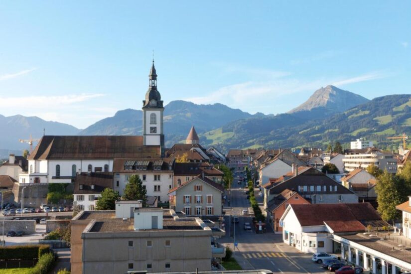 onde ficar em Gruyères na Suíça Uma pequena cidade europeia com uma torre de igreja, cercada por montanhas sob um céu azul claro.