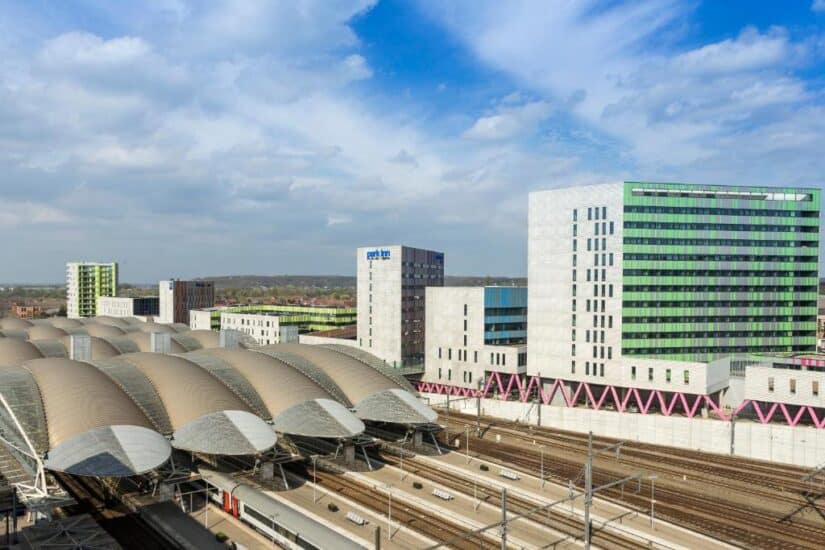 hotéis em Lovaina na Bélgica Estação de trem moderna com telhados em arco e prédios de escritórios altos adjacentes sob um céu parcialmente nublado onde ficar em Lovaina.
