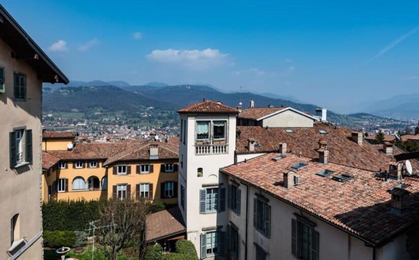 hotéis na citta alta em Bérgamo na Itália Prédios de telhado vermelho onde ficar em Bérgamo com vista para a montanha sob um céu azul brilhante em uma cidade europeia.