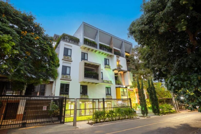 onde ficar em Cali na Colômbia Edifício moderno de vários andares com varandas, vegetação e uma entrada fechada em uma rua arborizada ao anoitecer.