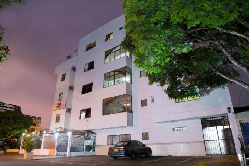 hotéis em San Fernando em Cali na Colômbia Um prédio onde ficar em Cali de apartamentos branco de quatro andares com grandes janelas, árvores e um carro estacionado ao anoitecer.