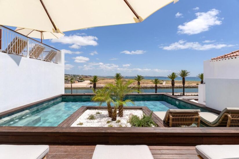 onde ficar em Lagos em Portugal Piscina moderna com palmeiras, espreguiçadeiras e vista para o mar sob um céu azul claro e guarda-sóis.